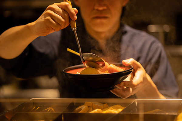 椀におでんを盛り付ける制服姿の店員の画像